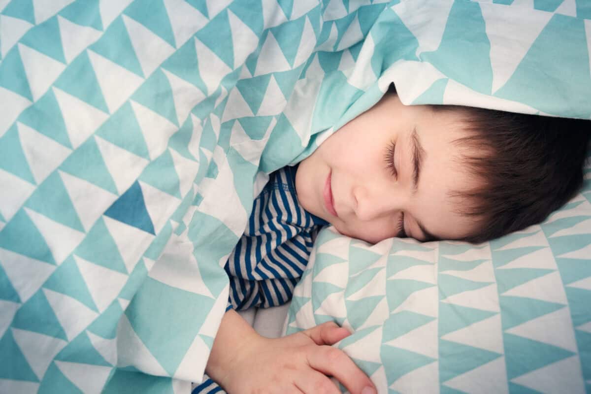 Un enfant de huit ans endormi dans son lit, la tête posée sur un oreiller