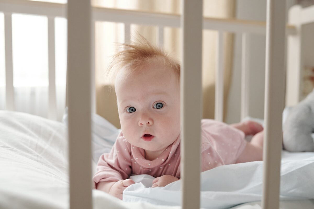 Cute infant girl in pink clothes crowling in her cradle