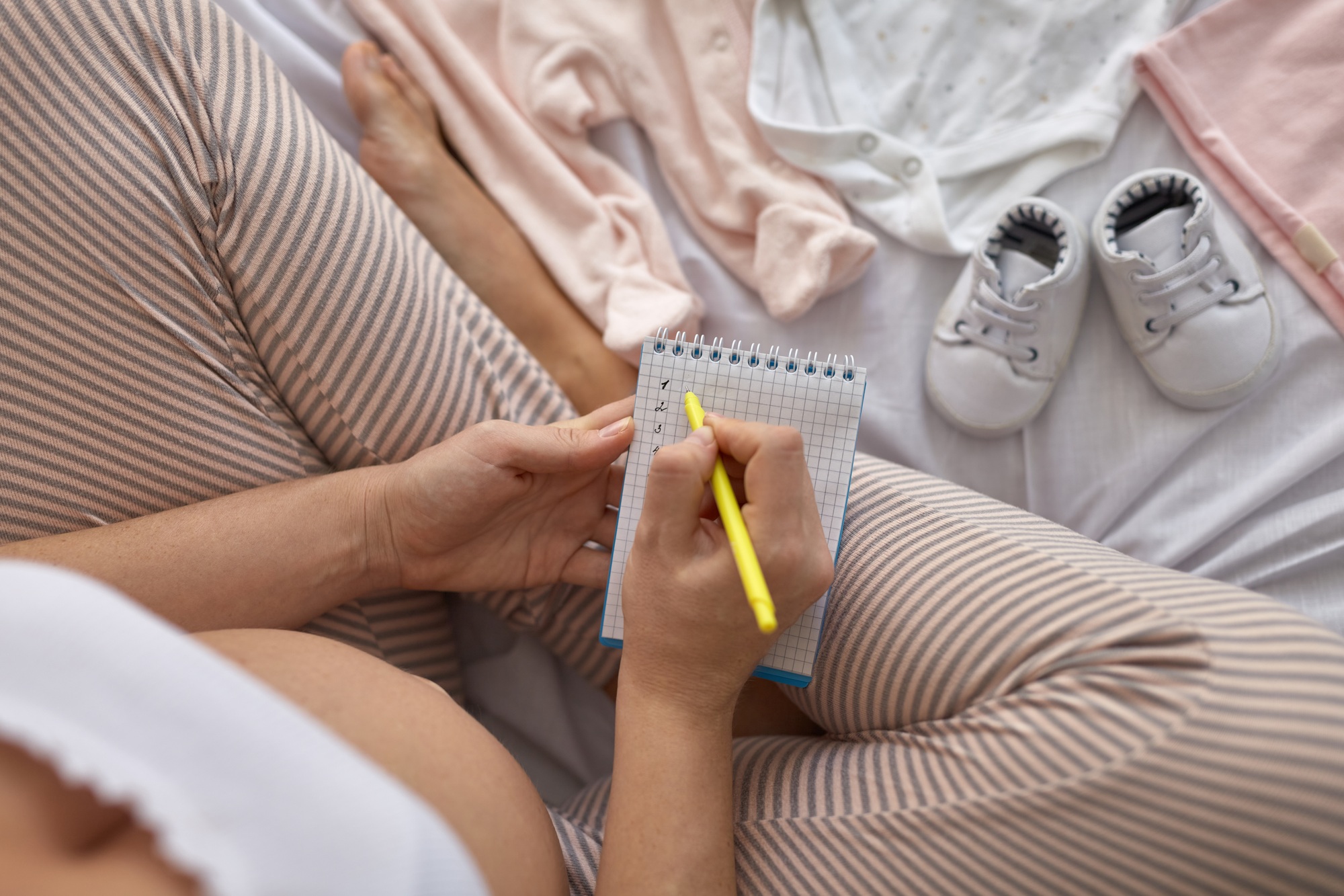 Vue de dessus d'une femme enceinte dans un lit préparant les vêtements de bébé à la maison